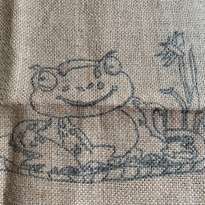 May include: A burlap bag with a black and white illustration of a frog sitting on a lily pad with a flower stem behind it.