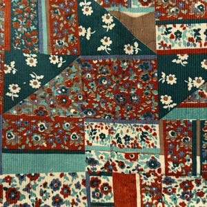 May include: Close-up of a patchwork fabric with a variety of floral patterns. The fabric features a mix of colors, including teal, red, and white, arranged in geometric shapes. The texture appears to be corduroy.