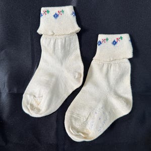 Könnte beinhalten: Ein Paar weiße Kniestrümpfe mit einem floralen Stickmuster in Rot, Blau und Grün.