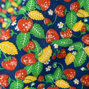 May include: A blue fabric with a repeating pattern of red strawberries, green leaves, and yellow leaves.