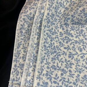 May include: A stack of white fabric with a blue floral pattern. The fabric has the text "Wm.sutta Div. of M. Lowenstein Corp." printed on the side.