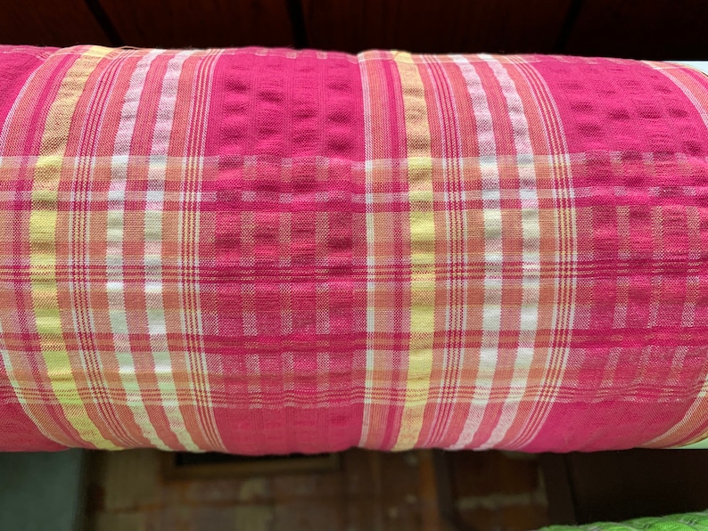 May include: Red, white, and yellow plaid fabric with a textured surface.