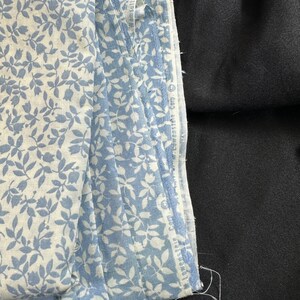 May include: A stack of blue and white fabric with a floral pattern. The fabric is folded and the edges are visible. The fabric is on top of a black surface.