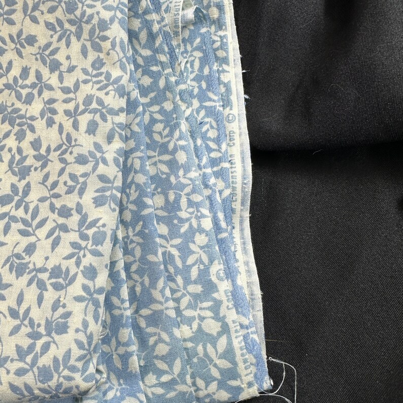 May include: A stack of blue and white fabric with a floral pattern. The fabric is folded and the edges are visible. The fabric is on top of a black surface.