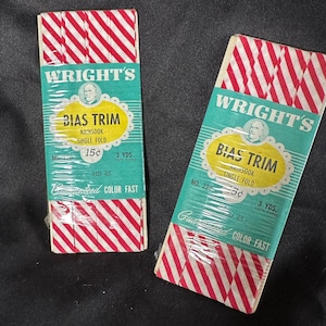 Op de afbeelding: Twee pakjes met rode en witte gestreepte biaisband, elk met het label "Wright's Bias Trim" met de tekst "Nainsoak Single Fold" en "3 yds. 100% Cotton". De pakjes zijn geprijsd met respectievelijk "15¢" en "5¢".