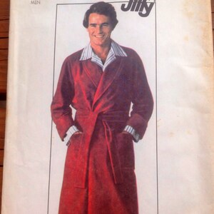 May include: Vintage Simplicity sewing pattern featuring a man in a burgundy robe with a shawl collar and a matching belt. The pattern is labeled "Jiffy" and includes the size "MEDIUM SIZE 38-40 MEN".