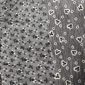 May include: Close-up of two fabric swatches. The left swatch has a textured, woven appearance with a pattern of small black floral and geometric shapes on a gray background. The right swatch features a pattern of black floral shapes and small circles on a gray background.