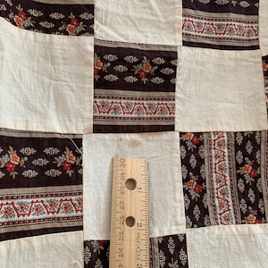 May include: A patchwork quilt with a brown and white pattern. The quilt is made of squares of fabric with different patterns. The fabric is a mix of brown, white, and red.