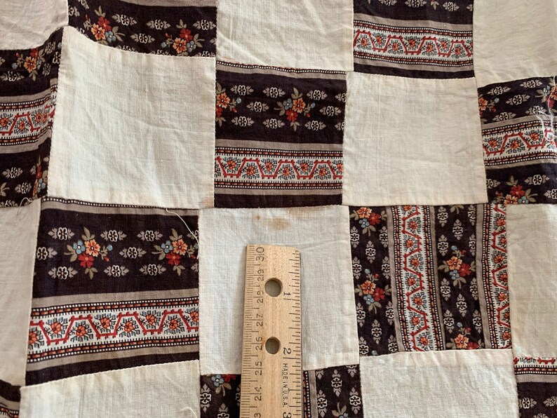 May include: A patchwork quilt with a brown and white pattern. The quilt is made of squares of fabric with different patterns. The fabric is a mix of brown, white, and red.