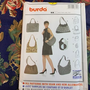 Può includere: Un pacchetto di modelli di cucito con vari design di borse. Il pacchetto mostra diversi stili di borse, tra cui borse tote, borse a tracolla e borse con coulisse. Il marchio "burda" è visibile in alto. Lo sfondo è un motivo floreale.