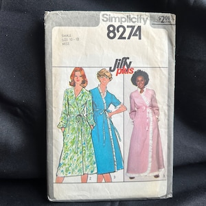 May include: Simplicity sewing pattern number 8274 for a Jiffy Plus wrap dress. The pattern is for sizes 10-12 and features three models wearing different versions of the dress. The dress is shown in a floral print, a solid blue, and a pink gingham.