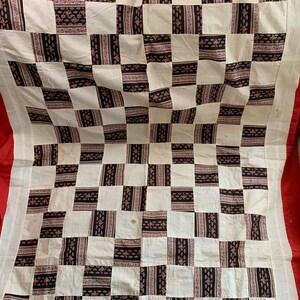 May include: A white and black checkered quilt with a red border. The quilt is made of fabric squares with a floral pattern.