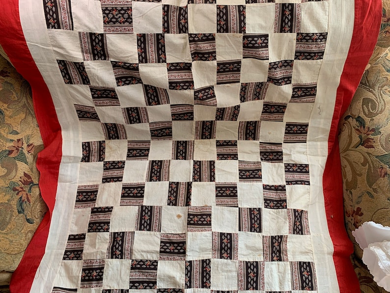 May include: A white and black checkered quilt with a red border. The quilt is made of fabric squares with a floral pattern.