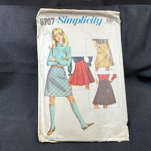 Könnte beinhalten: Simplicity Schnittmuster Nummer 6707 für einen Kinderrock. Das Schnittmuster enthält vier verschiedene Rockstile: einen karierten Rock, einen roten Faltenrock, einen braunen Rock und einen karierten Rock mit einem kiltartigen Design.