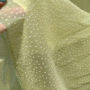 Puede incluir: Tela transparente de color amarillo pálido con un patrón de lunares blancos. La tela es translúcida y tiene una textura suave y delicada.