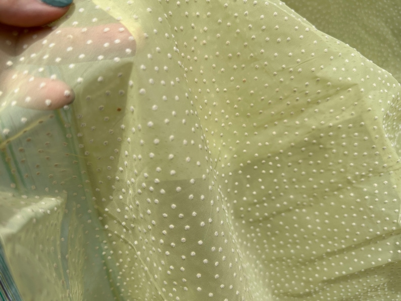 May include: Pale yellow sheer fabric with a white polka dot pattern. The fabric is translucent and has a soft, delicate texture.