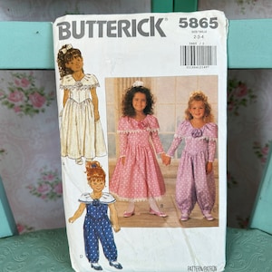 May include: Vintage sewing pattern for girls' dresses and overalls. The pattern is for sizes 2-4 and features a white dress with a lace collar, a pink dress with a lace collar and a purple overall with a lace collar. The pattern is from Butterick and the pattern number is 5865.