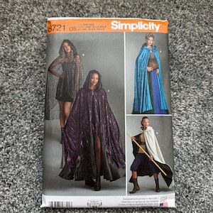 May include: Simplicity sewing pattern 8721 featuring hooded capes in various colors and styles. The pattern includes options for a black lace cape, a blue velvet cape, and a white and black cape. The pattern is one size and designed and printed in the USA.