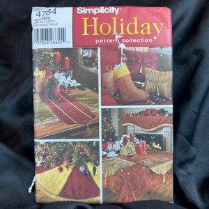 May include: Simplicity Holiday pattern collection sewing pattern with four different holiday table runner and tablecloth designs. The designs include a red and gold table runner, a red and gold tablecloth with a scalloped edge, a red and gold tablecloth with a scalloped edge and a Christmas tree design, and a red and gold tablecloth with a scalloped edge and a stocking design.