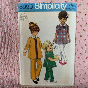 May include: A vintage Simplicity sewing pattern for children's clothing. The pattern number is 8990 and the price is 75 cents. The pattern includes two designs: a yellow dress with a white collar and a green dress with a white collar. The pattern is for size 3, with a 22-inch bust and a 20 1/2-inch waist.