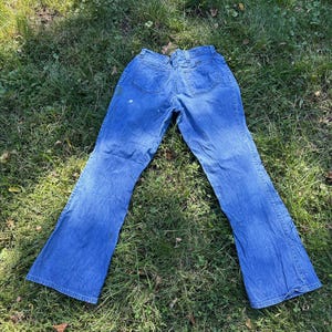May include: A pair of blue denim bell-bottom jeans with a slight fade. The jeans have a high waist and a wide leg opening.