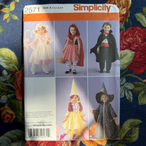 May include: Simplicity sewing pattern 2571 featuring children's costumes. The pattern includes designs for a Little Bo-Peep, Little Red Riding Hood, a vampire, a fairy, and a witch. The pattern is for sizes A 1/2, 1, 2, 3, and 4.