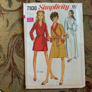 Può includere: Modello di cucito Simplicity numero 7930 per una vestaglia. Il modello è per taglie da donna 12-14 e include tre lunghezze diverse. La copertina del modello presenta tre modelle che indossano diverse versioni della vestaglia. La vestaglia a sinistra è rossa, la vestaglia al centro è a quadri gialli e neri, e la vestaglia a destra è bianca.