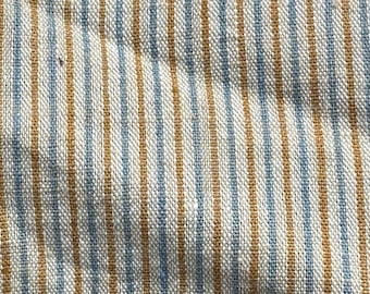 May include: Close-up of a white fabric with thin blue and brown stripes. The fabric has a woven texture.