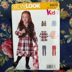 Può includere: Una busta per cartamodello New Look S0275 per abbigliamento per bambini. Il fronte mostra un bambino che indossa un vestito a quadri e un gilet in pelliccia sintetica marrone. Le illustrazioni mostrano varianti di gilet, vestiti e leggings.