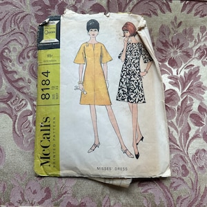 Könnte beinhalten: Vintage McCall's Schnittmuster für ein Damenkleid, Größe 12, Brustumfang 81 cm. Das Schnittmuster zeigt zwei Illustrationen einer Frau, die ein kurzärmliges Kleid trägt, eines in Gelb und eines in Schwarzweiß.