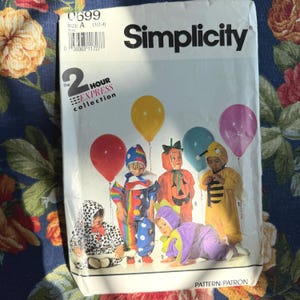 Może przedstawiać: Wzór szycia Simplicity 0699 dla kostiumów dziecięcych. Wzór zawiera różne kostiumy, w tym klauna, dynię, pszczołę i dalmatyńczyka. Opakowanie zawiera tekst "2 Hour Express Collection."