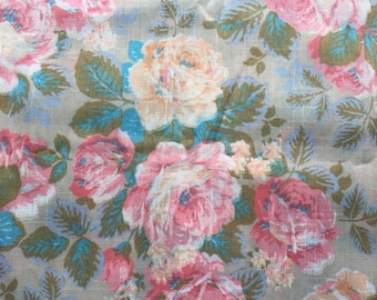 May include: A beige fabric with a floral pattern featuring pink, peach, and blue roses. The fabric has a textured linen-like appearance.