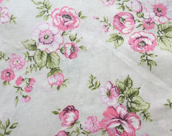 May include: White fabric with a repeating pattern of pink roses and green leaves. The floral design features various sizes of roses, with some in full bloom and others as buds. The fabric has a slightly textured appearance.