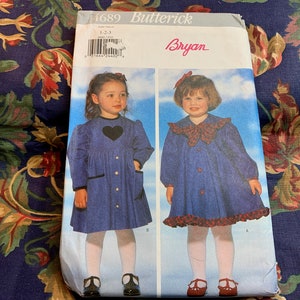 May include: A sewing pattern for a girl's dress, featuring two different styles. The pattern is from Butterick, and the design is by Bryan. The pattern is for sizes 1-2-3.