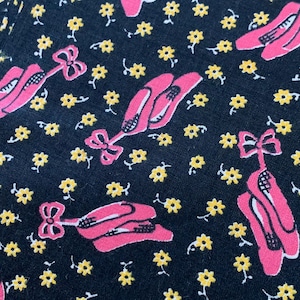 May include: Black fabric with a repeating pattern of pink ballet shoes with bows and yellow flowers.
