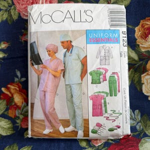 May include: A McCall's 9123 sewing pattern envelope for Uniform Essentials. The front shows illustrations of medical scrubs, including a V-neck top, trousers, and a lab coat in pink, green, and white. Text includes McCall's, Uniform Essentials, and 9123.