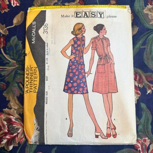 May include: Vintage McCall's sewing pattern envelope featuring illustrations of two dresses. One dress is blue with a floral pattern, the other is red gingham. The envelope has text that reads "A POUNDS-THINNER PATTERN" and "Make it EASY, please."