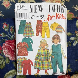 Può includere: Una busta per cartamodello New Look Easy for Kids 6664, taglia A 1/2, 1, 2, 3, 4. La busta di carta bianca presenta illustrazioni di abbigliamento per bambini, inclusi vestiti, tute e maglie a maniche lunghe in vari colori e fantasie.