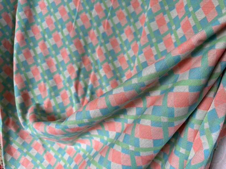 Puede incluir: Una tela a cuadros rosa y verde con textura tejida. La tela est&aacute; doblada y drapeada, mostrando el patr&oacute;n y la textura.