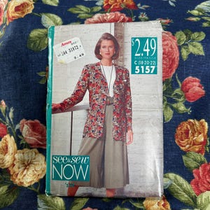 May include: A vintage sewing pattern packet featuring a woman in a floral jacket and skirt. The packet has the text "SEE & SEW NOW" and the price $2.49. The size is C (18-20-22). The packet is on a floral background.