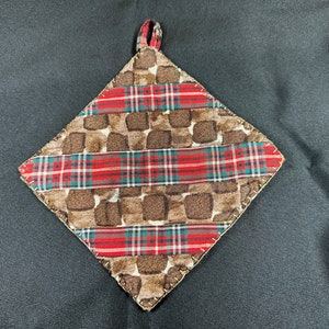 May include: A diamond-shaped pot holder with a brown and white patterned fabric and red and green tartan ribbon accents.