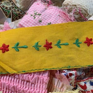 以下が含まれることがあります： 赤い刺繍の花と緑の葉が並んだ黄色の布のトリム