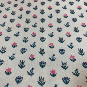 May include: White fabric with a repeating pattern of small pink and blue flowers with green stems. The flowers are stylized and have a simple design.
