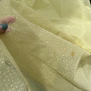 May include: Pale yellow sheer fabric with a white polka dot pattern. The fabric is slightly wrinkled and has a few brown spots.