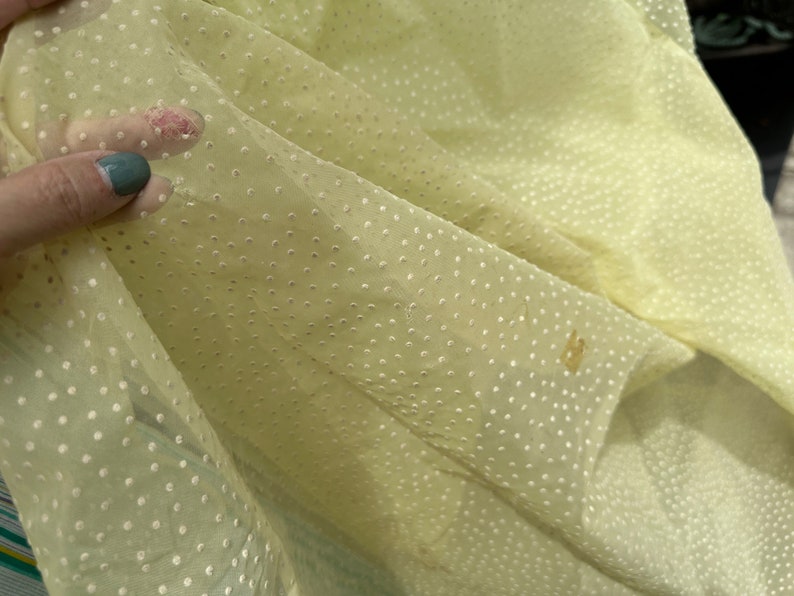 May include: Pale yellow sheer fabric with a white polka dot pattern. The fabric is slightly wrinkled and has a few brown spots.