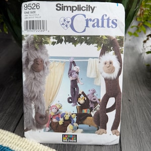 Puede incluir: Patrón de costura Simplicity Crafts con diseños de peluches de monos. El patrón incluye instrucciones para crear varios peluches de monos diferentes, con detalles sobre sus características y poses. La portada muestra los peluches terminados.
