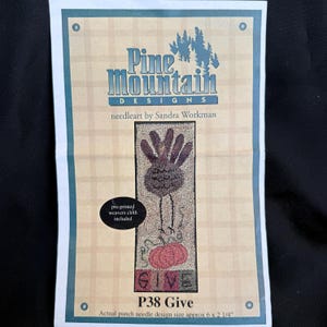May include: A package for a needleart project by Pine Mountain Designs. The design features a turkey and pumpkin with the word "GIVE". The actual punch needle design size is approximately 6 x 2.25 inches. Pre-printed weavers cloth is included.