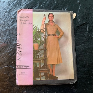 May include: A vintage McCall's Designer Collection sewing pattern for a dress. The pattern number is N/2749. The pattern is for sizes 10-18 and bust sizes 31-38. The pattern is pink and features a photo of a woman wearing a beige dress with a belt.