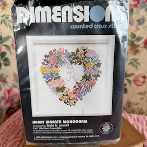 Peut inclure: Un kit de point de croix compté Dimensions avec un monogramme de couronne florale en forme de cœur. Le kit comprend du fil à broder en coton, une aiguille et des instructions. La taille du cadre est de 13x13cm.