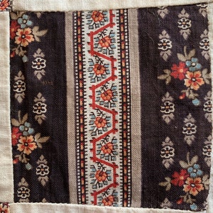 May include: A close-up of a fabric patchwork with a brown and white floral pattern, a red and white geometric pattern, and a beige background.
